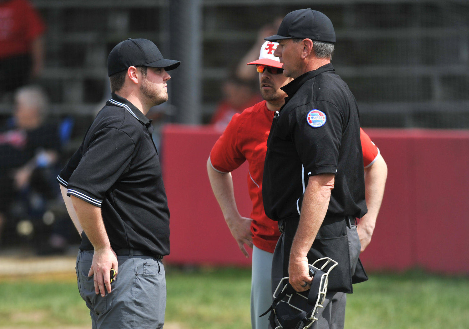 Connor Spunaugle, left, meets with Sacred Heart baseball head coach Jaric Reid and home plate umpire Brian Rice during a Kaysinger Conference Baseball Tournament game April 26 in Lincoln.